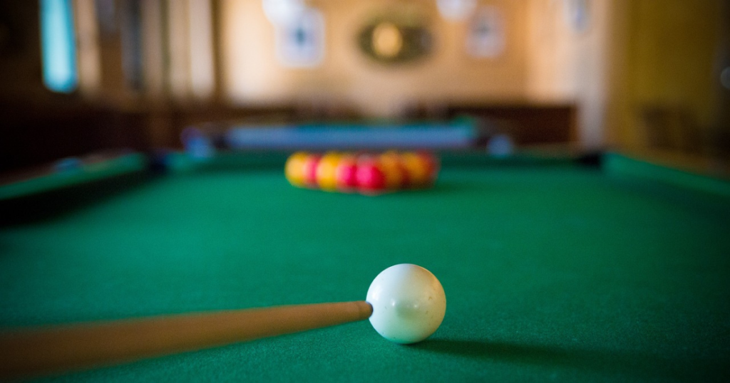 A white ball about to be struck by a cue into a fully racked pool ball set