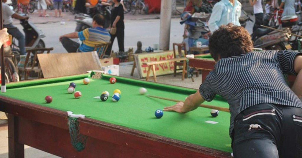 A man preparing to shoot the cue ball at a red pool ball